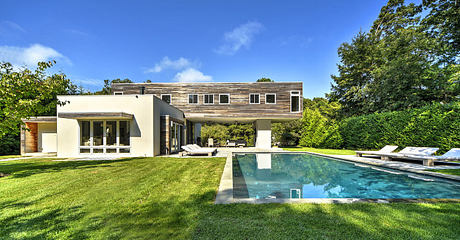 Modern home with wooden siding, large windows, and an inviting pool surrounded by lush greenery.