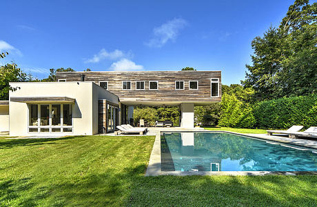 Modern home with wooden siding, large windows, and an inviting pool surrounded by lush greenery.