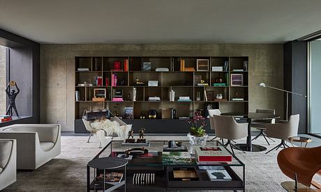 A modern and minimalist living room with concrete walls, custom shelving, and sleek furnishings.