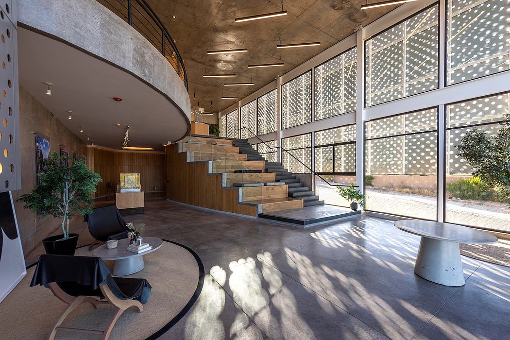 Spacious modern lobby with concrete walls, curved staircase, and perforated screen windows.
