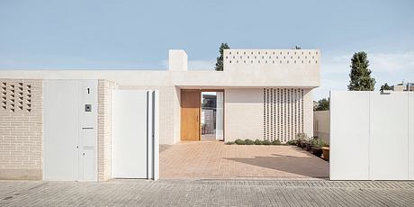 Minimalist exterior with brick facade, wooden front door, and patterned trellises.