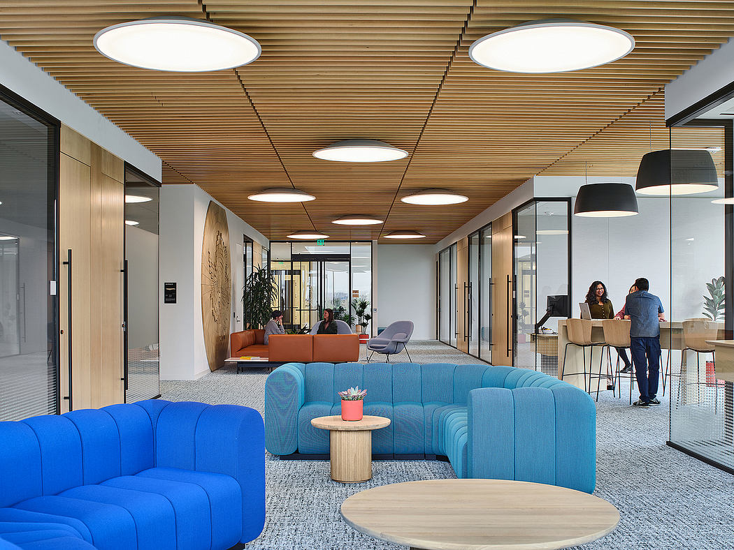 Spacious modern office interior with wooden ceiling, circular lighting, and colorful furniture.