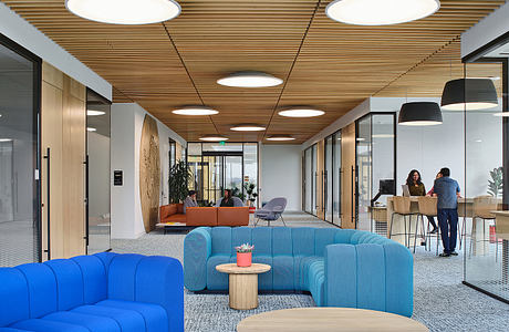 Spacious modern office interior with wooden ceiling, circular lighting, and colorful furniture.