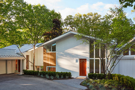 A modern, minimalist home with a striking red entrance door, surrounded by lush greenery.