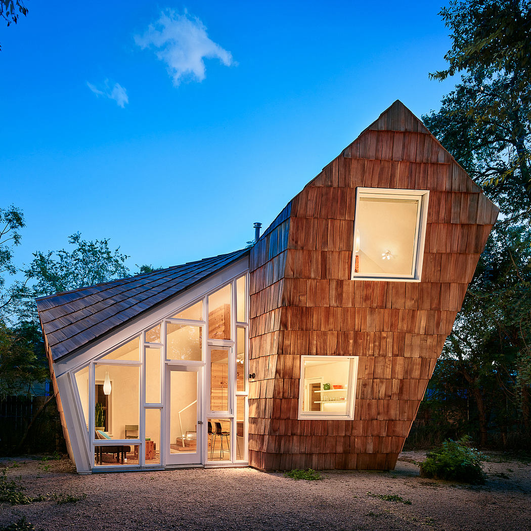 A modern wooden cabin with unique angular roof and large windows showcasing its interior.
