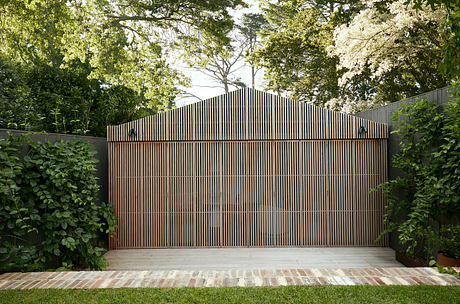 A modern wooden pavilion structure with a slanted roof surrounded by lush greenery.