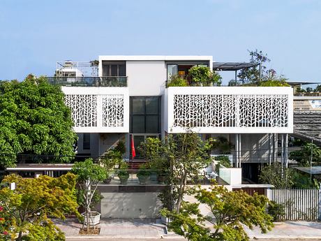 Modern multi-story building with intricate lattice balconies, surrounded by lush greenery.