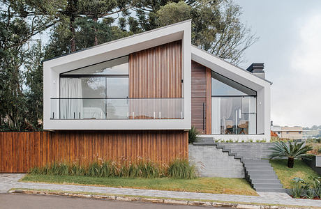 A modern, sleek house with a wooden exterior, large windows, and a balcony overlooking lush greenery.