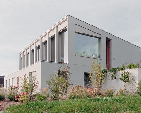 A modern, rectangular building with large windows and a lush, landscaped garden in the foreground.