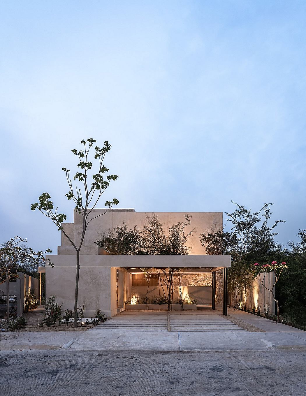A modern, minimalist building with a warm, inviting exterior featuring trees and lighting.