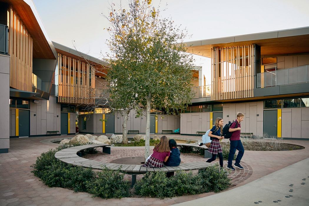 This image depicts a modern outdoor courtyard with a central tree, seating areas, and distinctive architectural design elements.