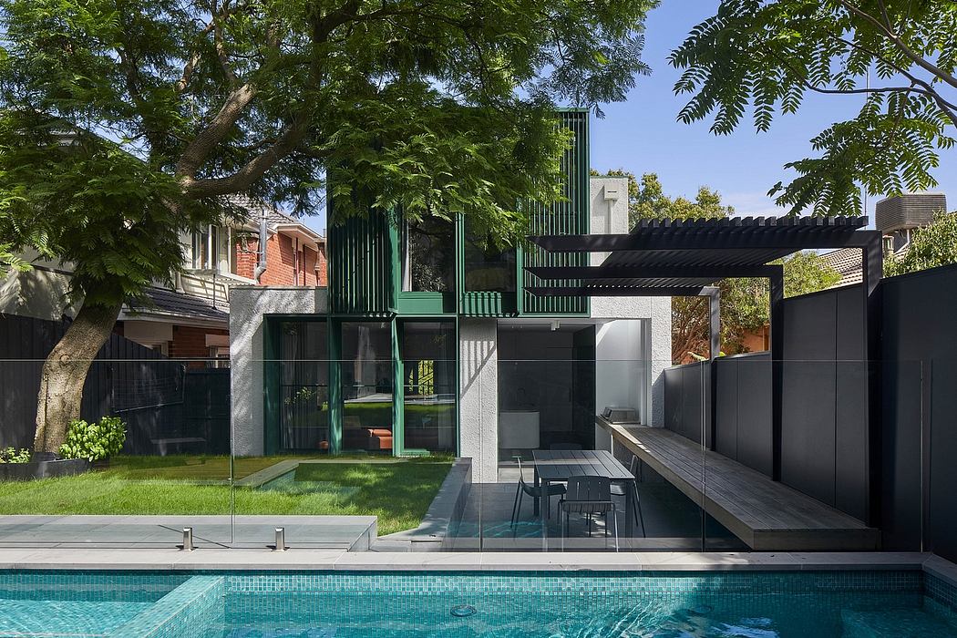 Modern architectural structure with sleek black and green metal elements, glass, and decking surrounding an inviting pool.