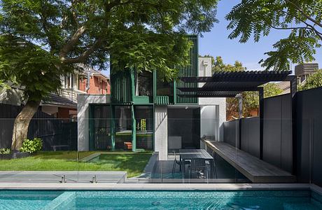 Modern architectural structure with sleek black and green metal elements, glass, and decking surrounding an inviting pool.