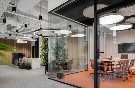 Modern office space with glass walls, circular lighting fixtures, and natural elements.