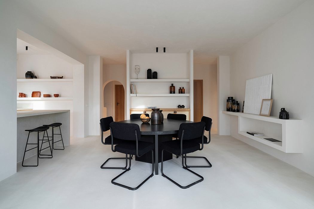 Spacious, minimalist dining area with sleek black chairs, shelves, and open kitchen.