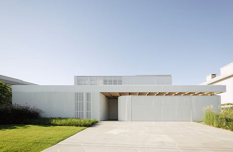 Clean, minimalist exterior with wooden canopy, paved courtyard, and lush greenery.