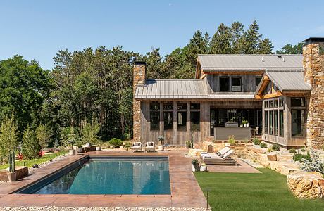 A rustic modern mountain home with a pool, stone and wood exterior, and lush landscaping.