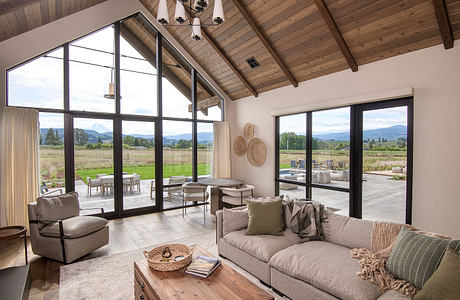 Rustic cabin-style interior with vaulted ceiling, exposed wood beams, and expansive windows offering scenic mountain views.