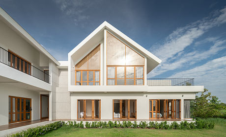 Modern architecture with gabled roof, large windows, and sleek white exterior. Lush landscaping and balconies complement the minimalist design.