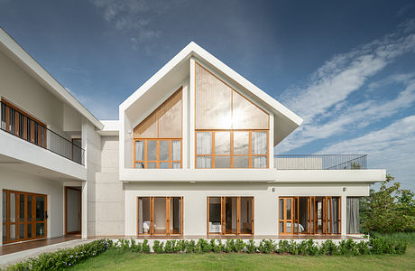 Modern architecture with gabled roof, large windows, and sleek white exterior. Lush landscaping and balconies complement the minimalist design.