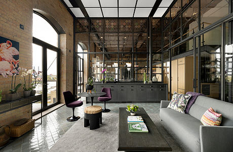 A modern and stylish industrial-inspired living space with glass walls, minimalist furnishings, and botanical accents.