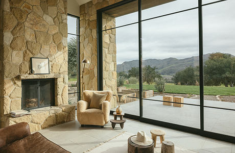 Cozy stone-walled living room with floor-to-ceiling windows offering mountain views.