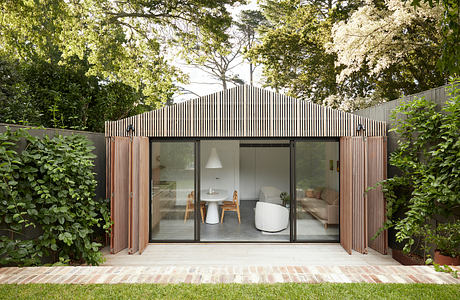 A modern, wooden structure with a peaked roof and large glass windows, surrounded by lush greenery.