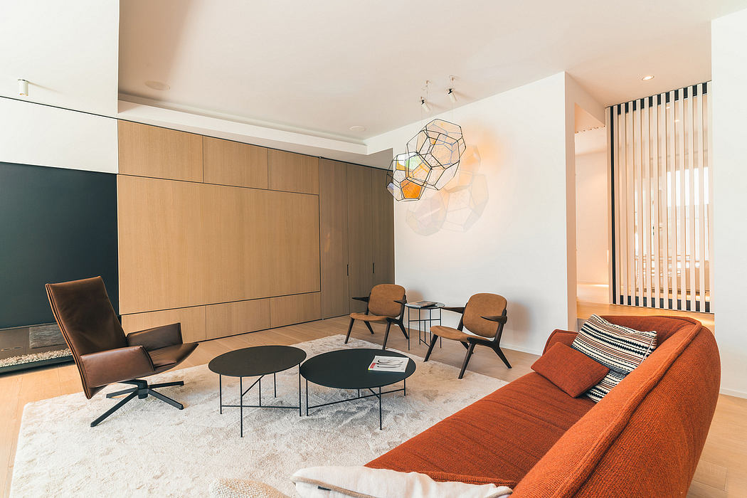 Modern, minimalist living room with warm wood cabinetry, geometric lighting, and a cozy orange sofa.