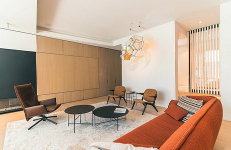 Modern, minimalist living room with warm wood cabinetry, geometric lighting, and a cozy orange sofa.