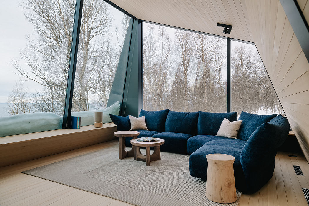 Modern living space with floor-to-ceiling windows showcasing natural scenery and plush blue sofa.