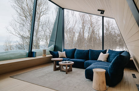 Modern living space with floor-to-ceiling windows showcasing natural scenery and plush blue sofa.