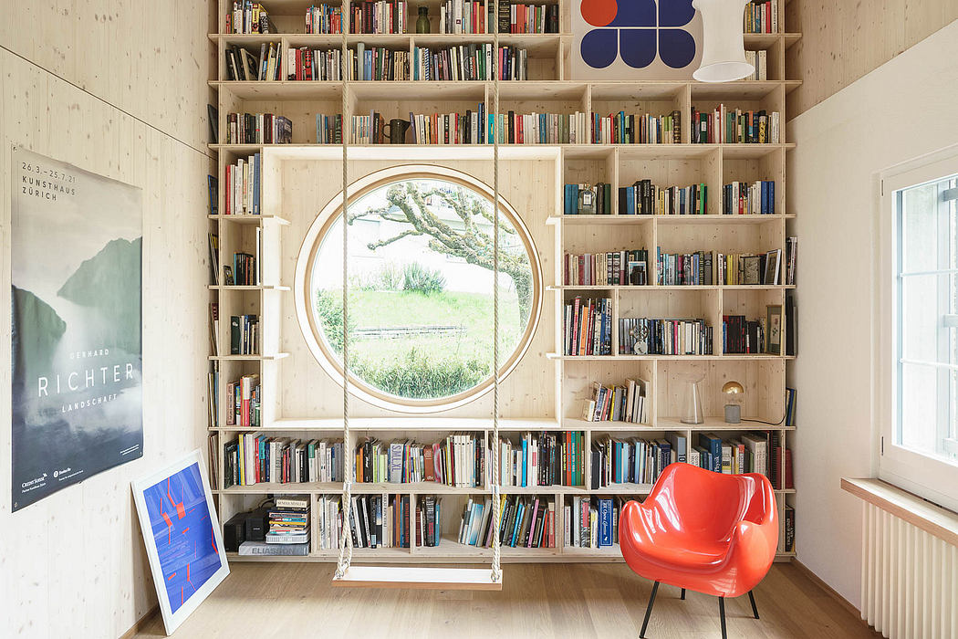 Cozy home library with circular window, wooden shelves, and vibrant red chair.