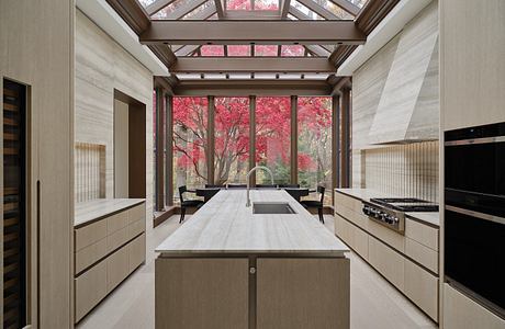 A modern kitchen with a glass-paneled ceiling framing vibrant fall foliage outside.