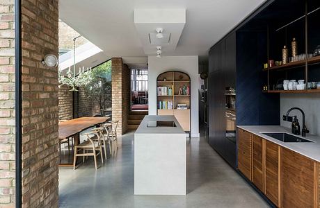 A modern kitchen with sleek black and wood cabinetry, concrete floors, and an arched entryway.