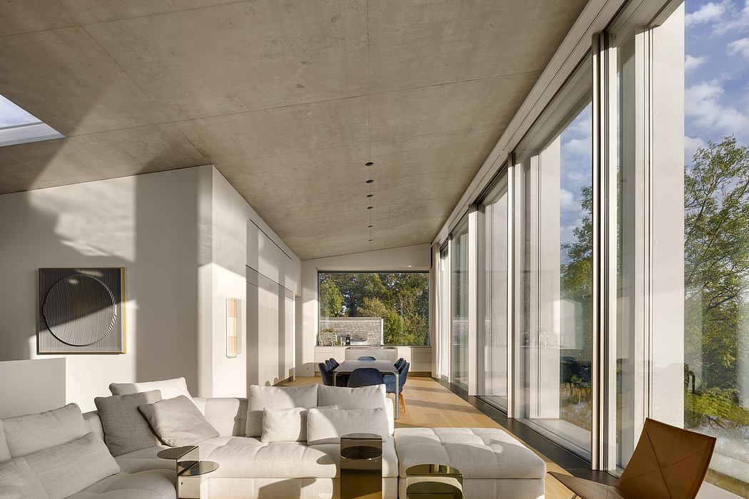Spacious modern interior with large windows, minimalist furniture, and concrete ceiling.