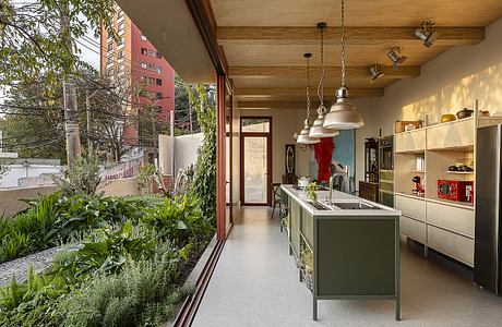 A modern, open-concept kitchen with wood-paneled ceilings, pendant lights, and a garden view.