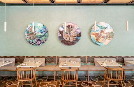 A modern restaurant interior with wooden tables, chairs, and colorful circular wall decor.