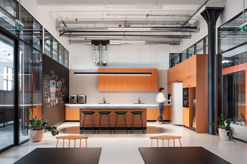 Stylish modern office kitchen with sleek orange cabinetry, minimalist decor, and industrial lighting.