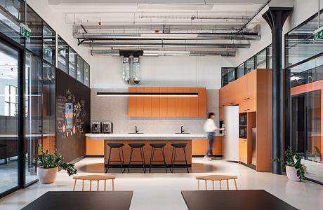 Stylish modern office kitchen with sleek orange cabinetry, minimalist decor, and industrial lighting.