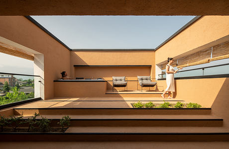 Modern, sunlit interior with geometric architecture, built-in shelving, and a person on the balcony.