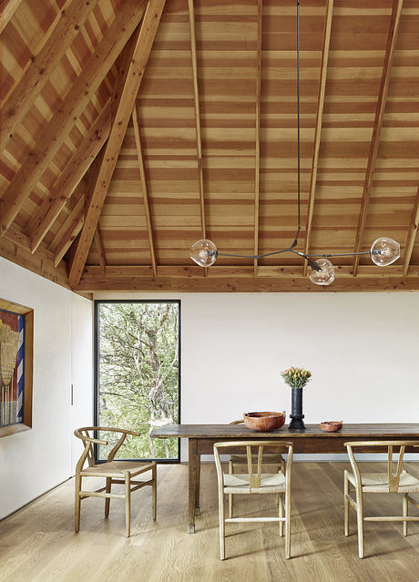 Rustic wooden ceiling beams, modern pendant lighting, and a large window frame a cozy dining space.