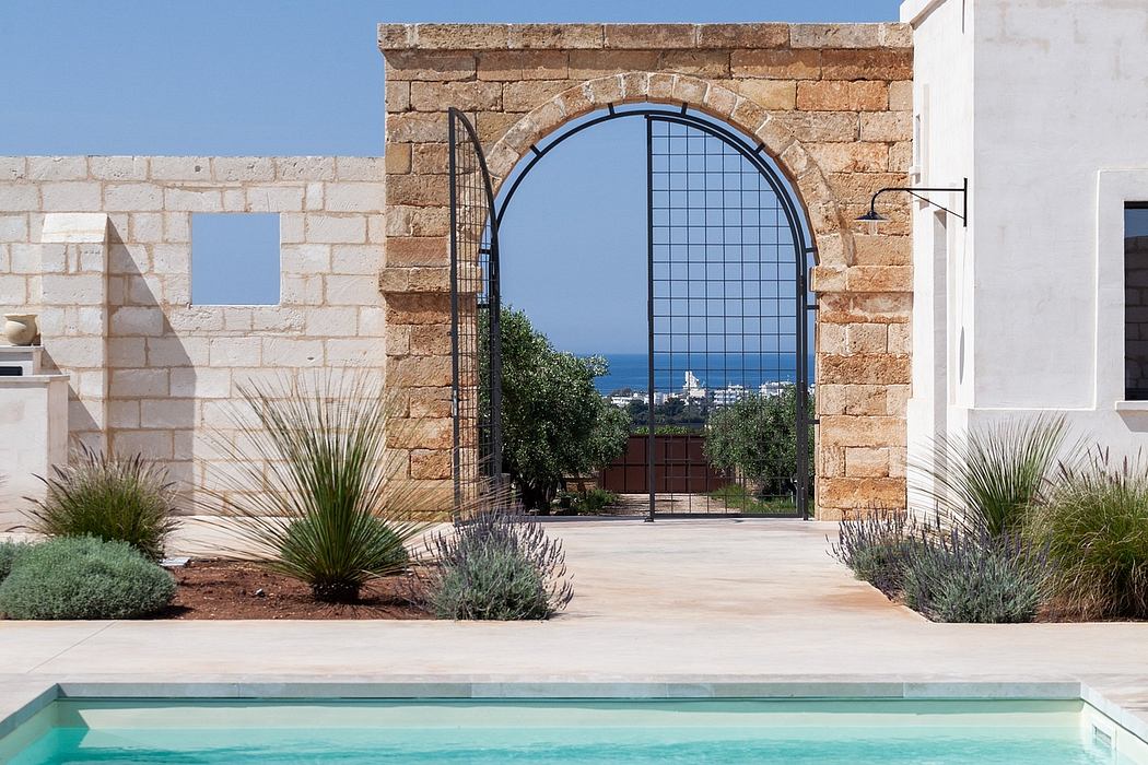 A stately stone archway framing a stunning ocean view, surrounded by lush desert landscaping.