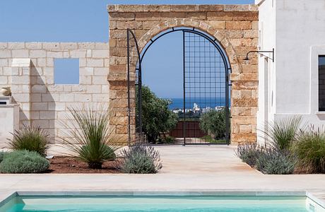 A stately stone archway framing a stunning ocean view, surrounded by lush desert landscaping.