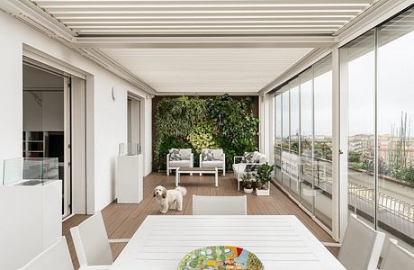 A bright and modern balcony with lush vertical garden, large windows, and cozy seating.