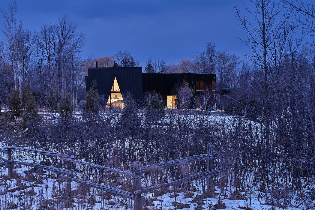 Modern, geometric cabin nestled in a snowy forest, warm lights glowing through its angular windows.