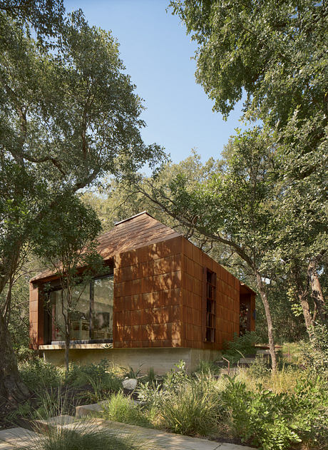 A modern wooden cabin nestled in a lush, verdant forest, featuring a sleek, geometric design and large windows that allow natural light to flood the interior.