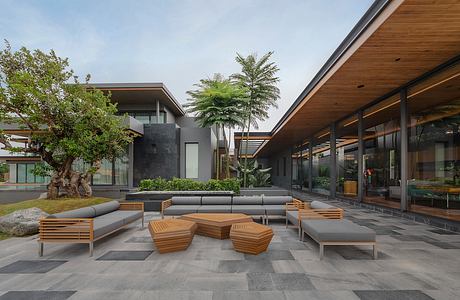 Contemporary outdoor lounge area with wooden benches, planters, and glass walls.