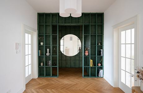 Minimalist room with green metal shelving unit and round mirror, parquet flooring.