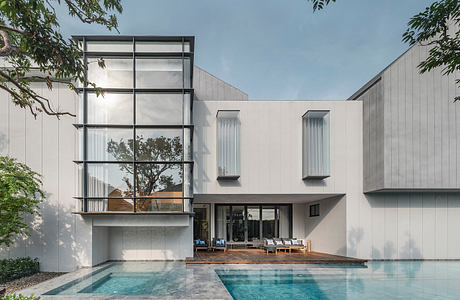 A modern residential building with a sleek, minimalist design, featuring a pool and lush greenery.