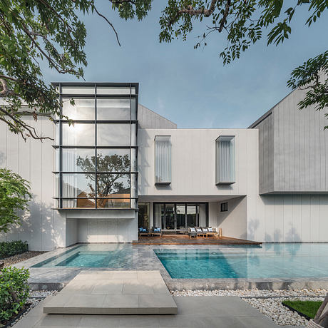 A modern residential building with a sleek, minimalist design, featuring a pool and lush greenery.